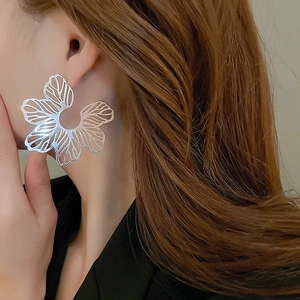 Close-up of oversized silver hollow flower earrings worn by a model in a profile view