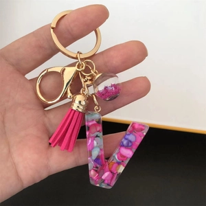 Detail of resin letter V keychain with pink shell flakes, gold ring and tassel