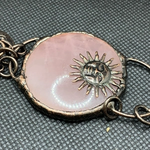 Close-up of vintage bronze sun deity pendant featuring a rose quartz stone inlay