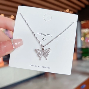 Macro view of a silver butterfly pendant necklace with inlaid white crystals on a card