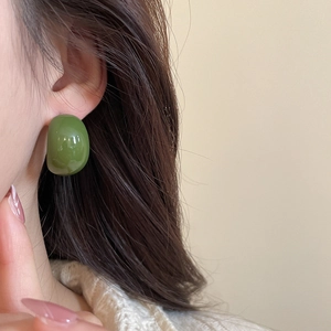 Close-up of a model wearing minimalist green acrylic C-shaped earrings with a glossy finish