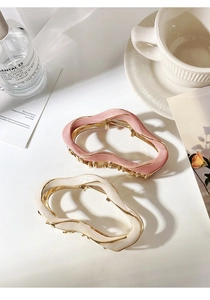 Detailed view of pink and beige enamel wavy metal hair claws on a stylish table