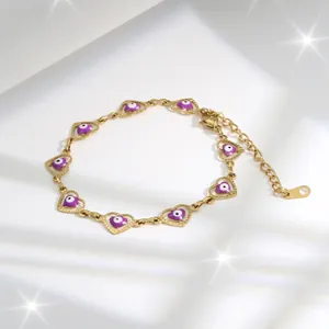 Detailed close-up of golden heart chain bracelet with purple evil eye charms on white silk