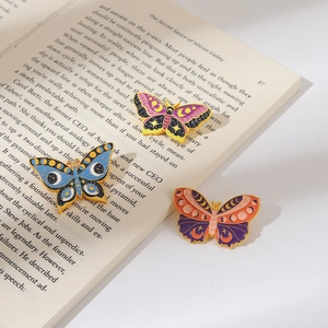 Three colorful butterfly enamel pins with moon and star patterns on vintage book