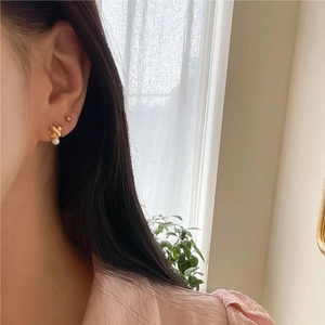 Close-up of golden knot stud earring with pearl accent on model by window
