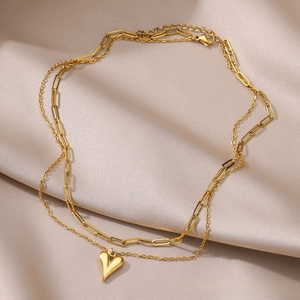 Detail of layered gold heart pendant necklace with trendy paperclip chain on silk fabric