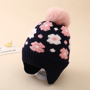 Close-up of navy knit winter hat for girls with flower patterns and a pink faux fur pompom
