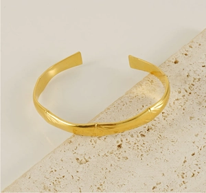 Detail view of gold C-shaped bamboo texture cuff bracelet on a natural stone surface