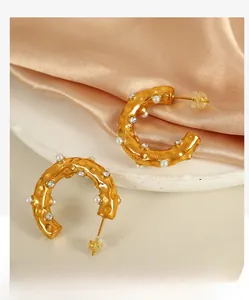 Close-up of C-shaped 18K gold earrings with hammered texture and pearl zircon inlay
