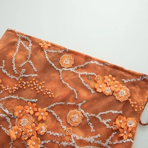 Detailed close-up of orange mesh fabric with 3D floral embroidery, sequins and pearls