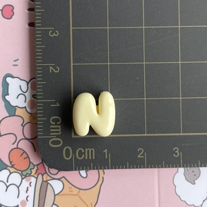 Mini yellow resin letter N charm shown on a measurement grid for size reference