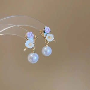 Détail de boucles d'oreilles fleuries avec pétales roses et blancs et perles élégantes