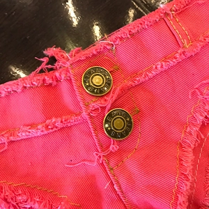 Dettaglio di pantaloncini di jeans rosa con bordi sfrangiati e bottoni dorati vintage con logo
