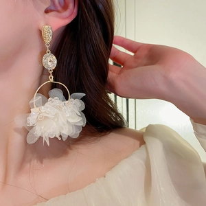 Detail view of long gold flower earrings with white fabric petals and crystals