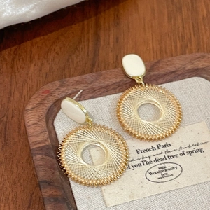 Gros plan de boucles d'oreilles circulaires dorées avec clous ovales blancs sur bois
