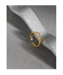 Detail of gold hammer textured ring with a rectangular clear zircon stone on a grey display