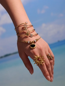 Vue détaillée du bracelet coeur émail doré et des bagues sur fond de plage d'été