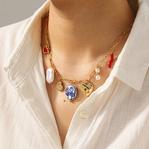 Detail of gold paperclip chain necklace with heart, pearl, and seashell charms on model