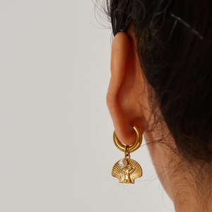 Close-up of gold shell drop earrings with goddess relief and white pearl detail