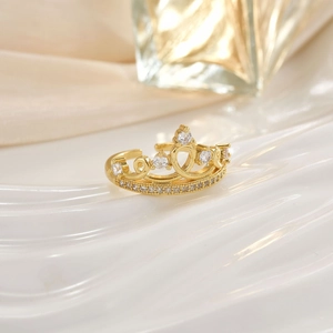 Detailed close-up of golden crown ring with micro-pave crystals on soft white surface