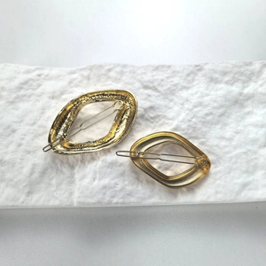 Set of two gold geometric oval hair clips on a white textured stone surface