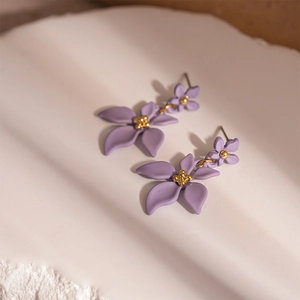 Détails de boucles d'oreilles fleurs mauves à deux couches avec étamines dorées sur fond blanc