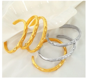 Detailed view of irregular hammered metal bangles in gold and silver on white fabric