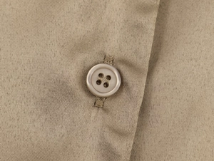 Détail de la texture du tissu en soie kaki et du bouton assorti sur la chemise