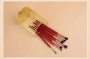Deep red makeup brush set with gold metal holder on a warm apricot background