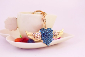 Close-up of golden winged heart keychain with blue rhinestones on a decorative saucer