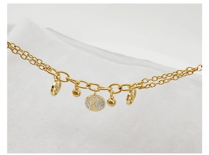 Detail of 18K gold-plated double-layered chain bracelet with polished beads and medallion