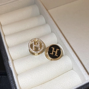 Macro detail of gold-plated H-logo earrings with inlaid crystals and black enamel finish