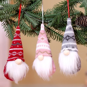 Close-up of knit Christmas faceless gnomes hanging on tree branches in red and pink
