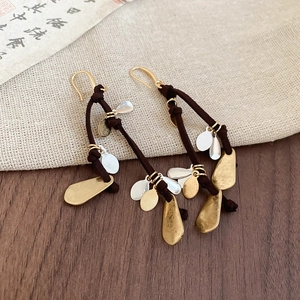 Detail of long fringe drop earrings with gold and silver waterdrop sequins on wood
