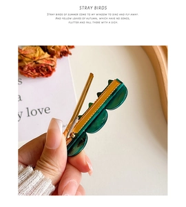 Close-up of emerald green acetate hair clip with gold metal base and marble texture