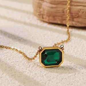 Macro shot of a minimalist gold necklace featuring an emerald-cut green gemstone pendant