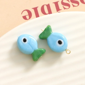 Macro shot of 3D blue and green glass fish charms with gold rings on white ceramic plate
