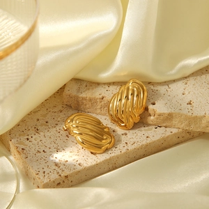 Dettaglio di orecchini a cerchio dorati con texture a spirale su pietra di travertino beige