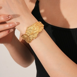 Dettaglio del bracciale rigido dorato irregolare martellato indossato su maglia nera