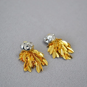 Detailed close-up of gold leaf tassels and silver irregular studs on a grey fabric background