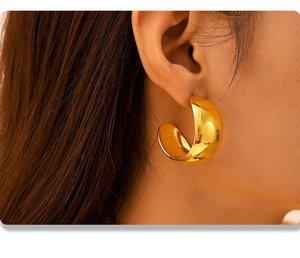 Close-up of a gold PVD coated wide C-shaped hoop earring on a female model