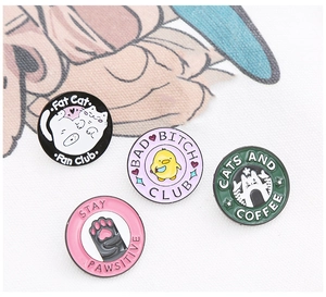 Detail of four colorful enamel lapel pins featuring various cat club designs and quotes