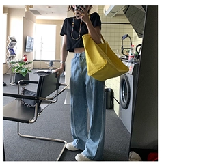 Detail view of yellow canvas tote bag held by model wearing blue jeans and black t-shirt