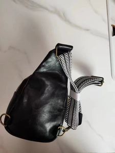 Detail of black pebbled leather chest bag with vintage bronze zipper and striped strap