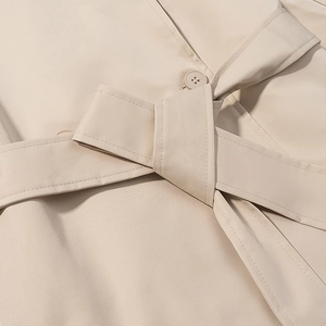 Dettaglio del nodo in vita e doppie cuciture su un trench corto beige