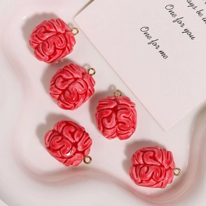 Macro detail of pink resin brain charms with golden metal loops on a pink tray