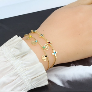 Dettaglio di braccialetti dorati sovrapposti con malocchio e ciondoli a fiore in smalto