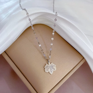 Detailed view of silver maple leaf pendant on a sequin chain over a golden jewelry box