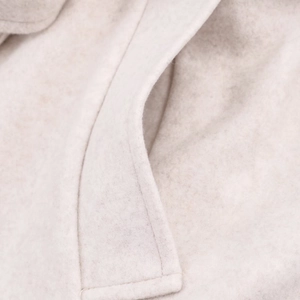 Macro shot of oatmeal wool coat fabric showing pocket stitching and soft texture