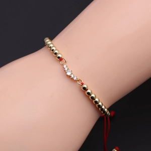 Detailed shot of red braided rope bracelet with gold beads and white zircon inlay